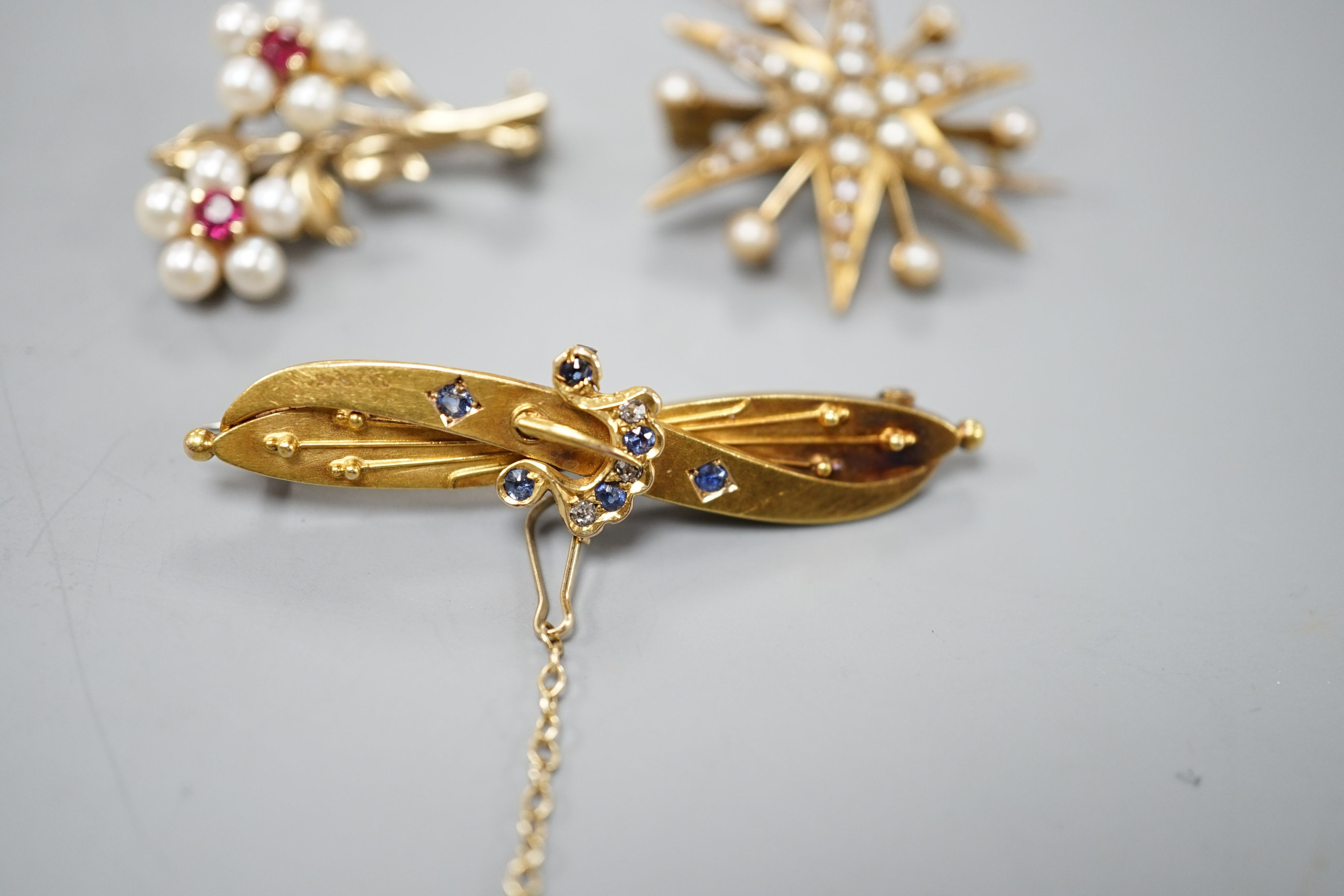 A late Victorian 15ct gold and sapphire set bar brooch, 44mm, gross weight 3.5 grams, an Edwardian yellow metal and split pearl set starburst brooch, gross weight 4.6 grams and a modern 9ct gold and gem set twin flower b